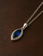 Mekik kesim mavi taşlı gümüş kolye ahşap zemin üzerinde yakın plan.